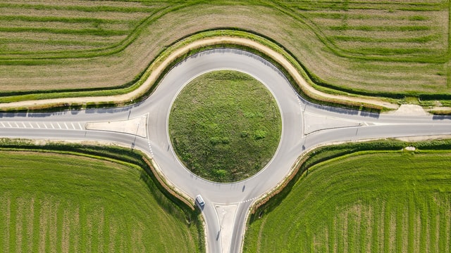 A top down view of a roundabout surrounded by green plains. This roundabout is a reminder of the northwest of CERN, but this one is prettier and probably safer.